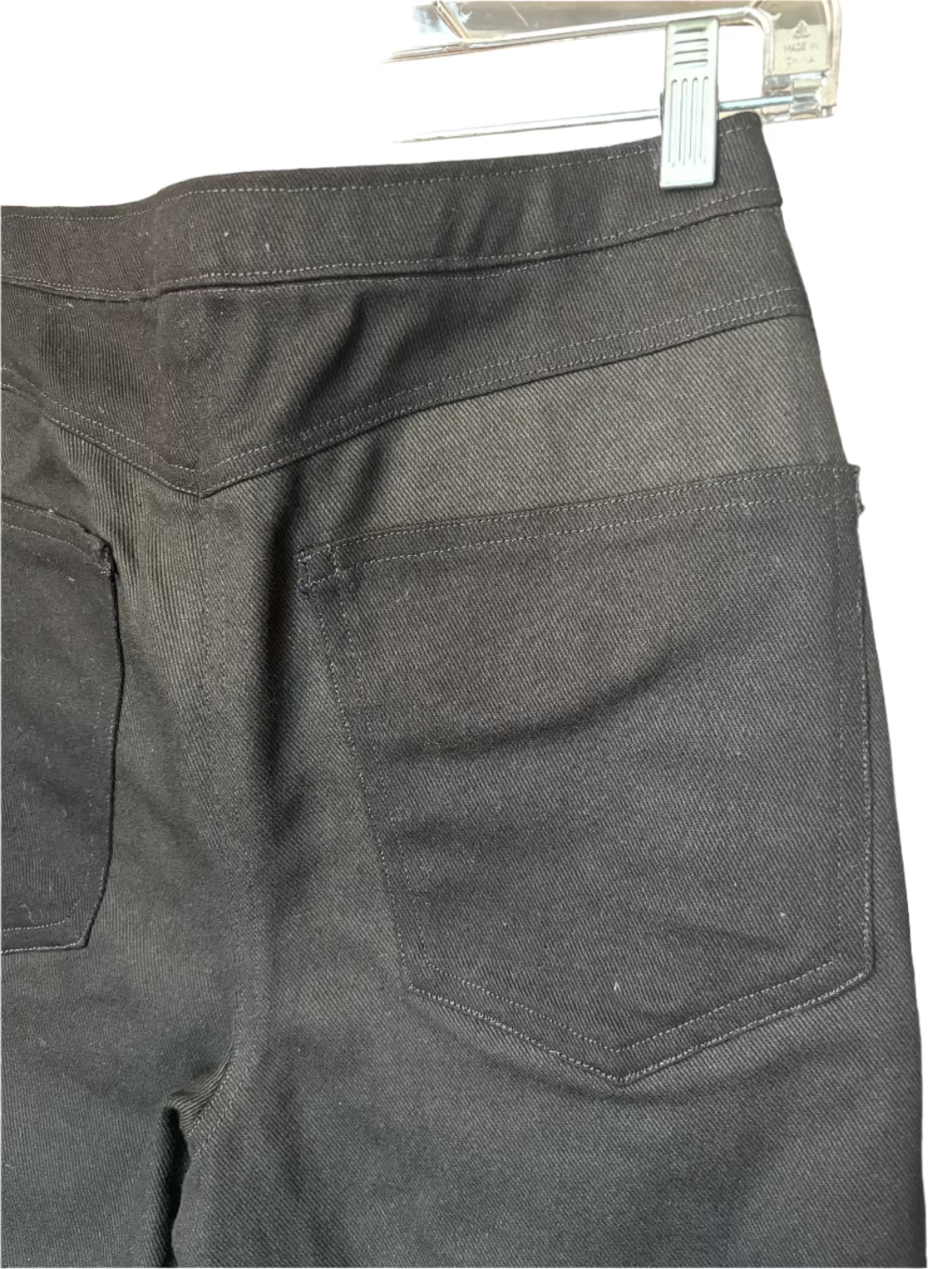 Black pants on a clear hanger against a beige background