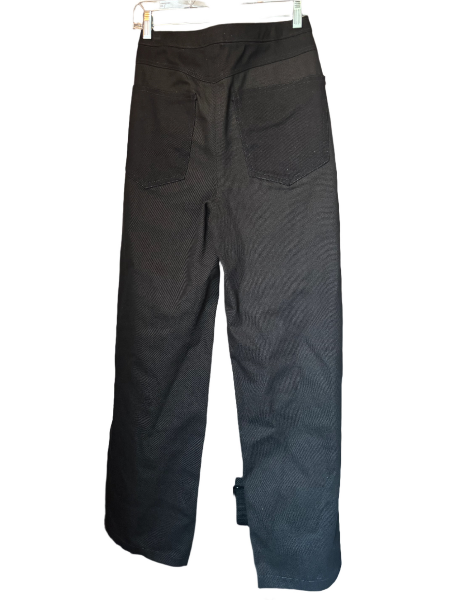 Black pants hanging on a rack against a neutral wall.