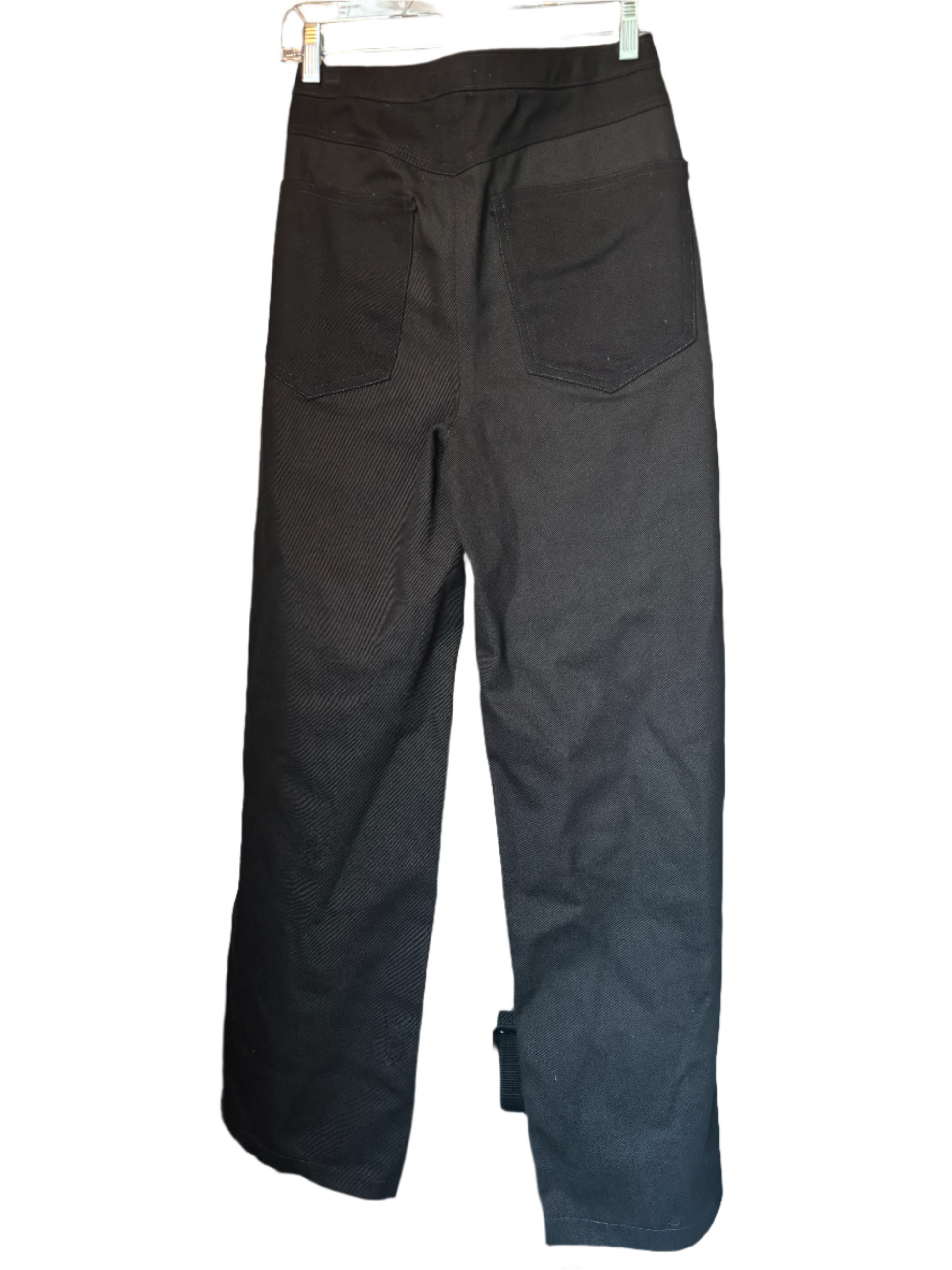 Black pants hanging on a rack against a neutral wall.