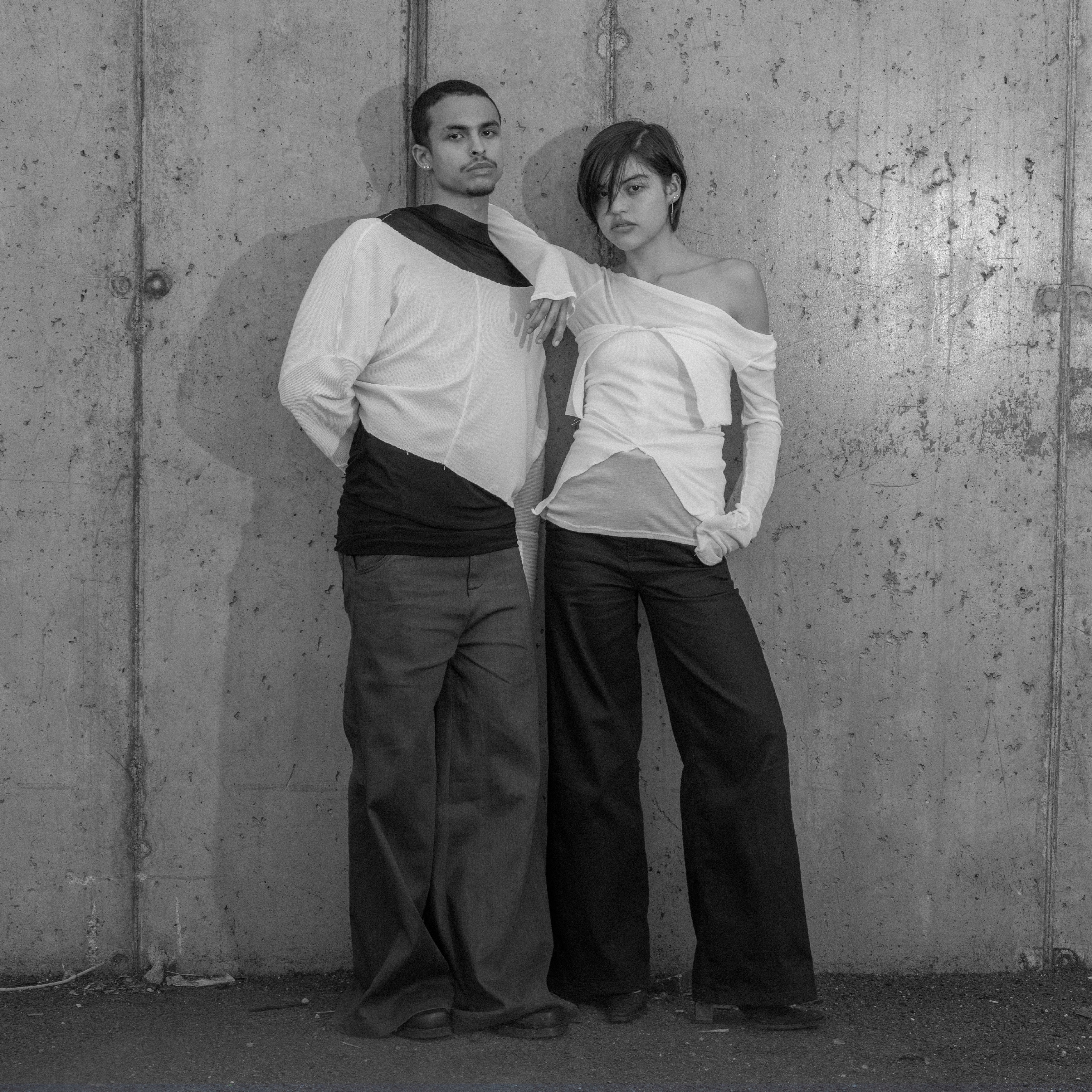 Two people posing against a textured wall.